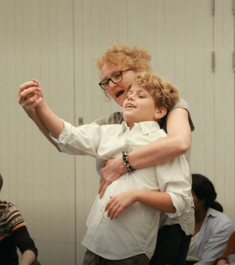 Kelly holding the hand of an autistic child in a Shakespeare adaption for autistic individuals using the Hunter Heartbeat method
